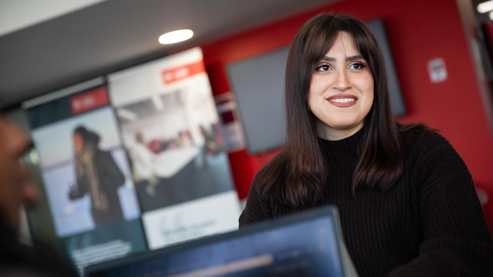 business student sat with laptop, smiling into distance