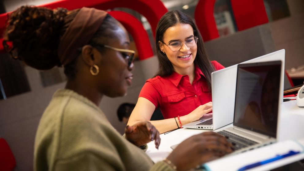 two students with their laptops sat smiling and talking