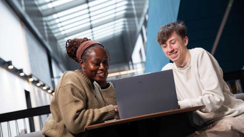 two students sat looking and smiling at laptop