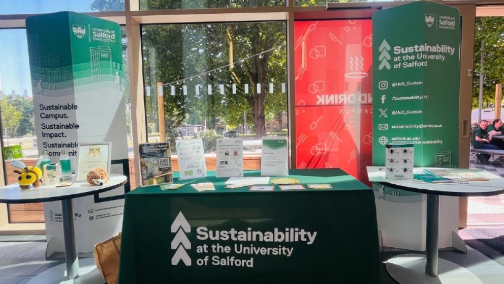 Display stand promoting the University of Salford's sustainability initiatives, highlighting a goal to create a sustainable campus and positive impact