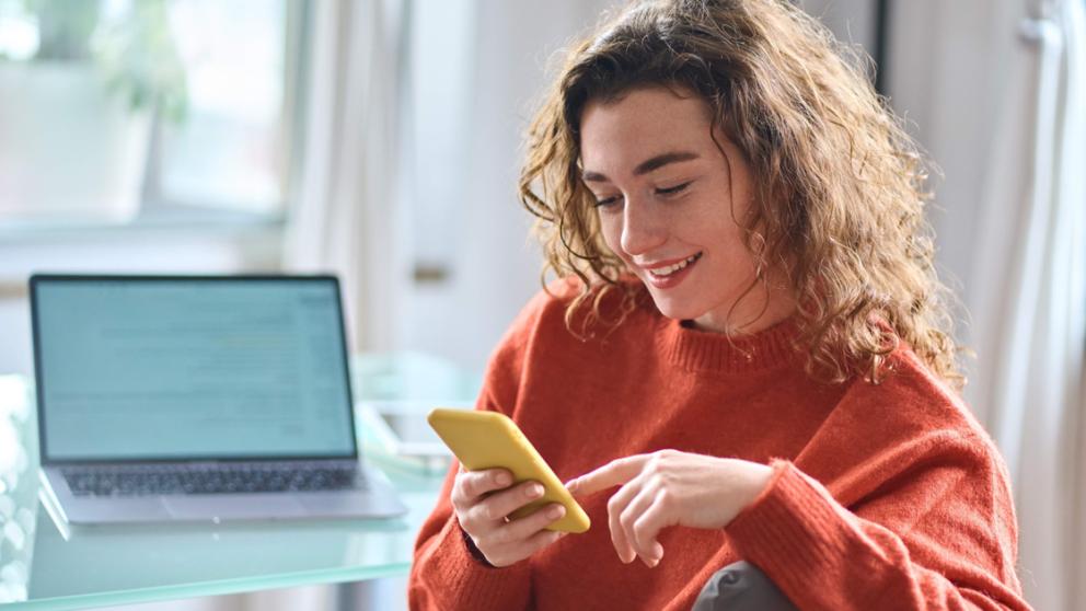 Woman using her smartphone besides a laptop on a table
