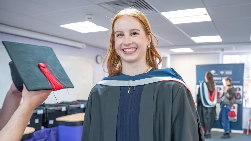 Graduand wearing traditional academic graduation attire, including gown and an academic hood