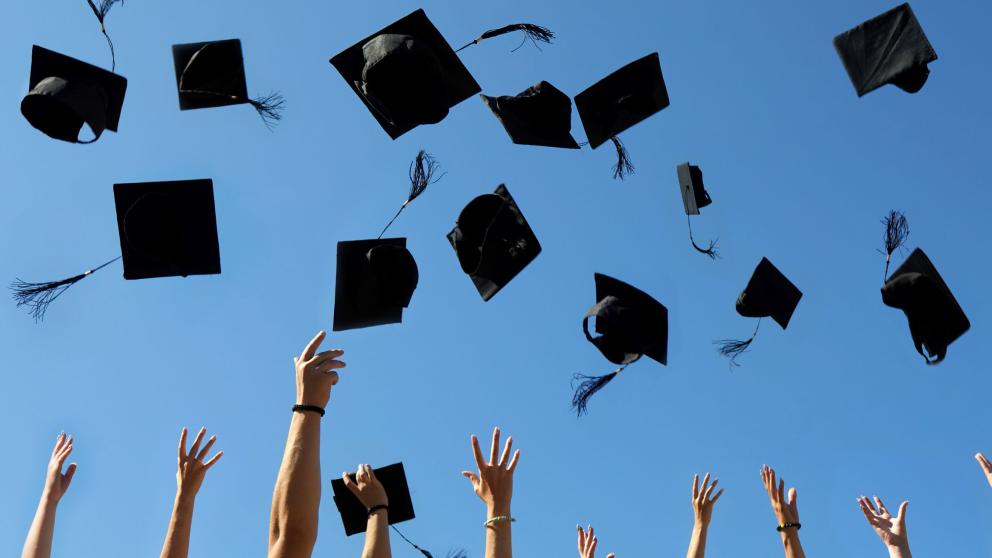 A wide shot of the arms of a group of people throwing graduation caps in the air