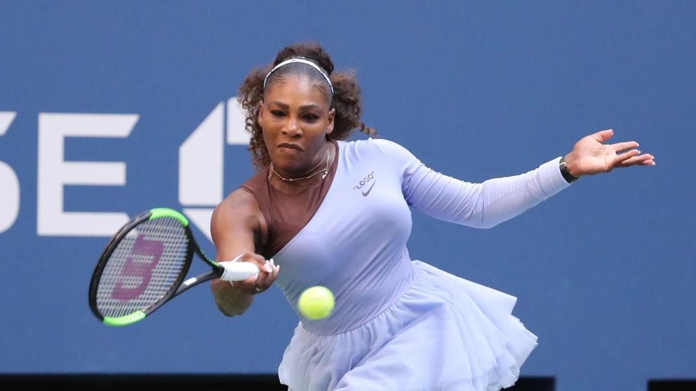 Serena Williams swings her racket towards the tennis ball with an expression of focused concentration