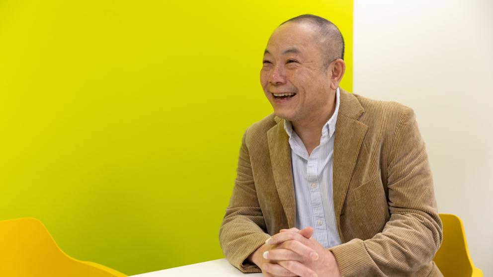 Colleague wearing a corduroy jacket seated in front of a bright yellow-green wall