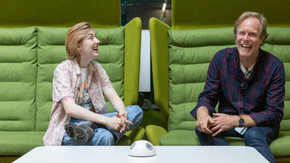 Two colleagues laughing together while seated in green acoustic office pods