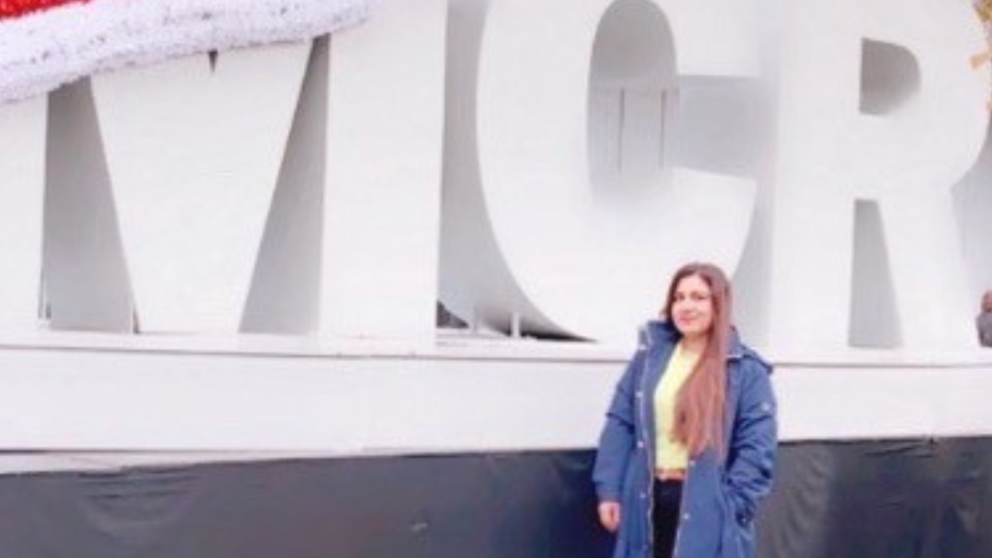 Sana standing in front of a christmas MCR sign in a coat, smiling