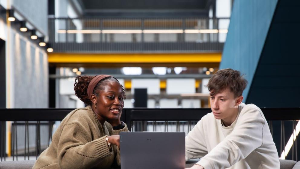 Students working together at a laptop in a campus building study space