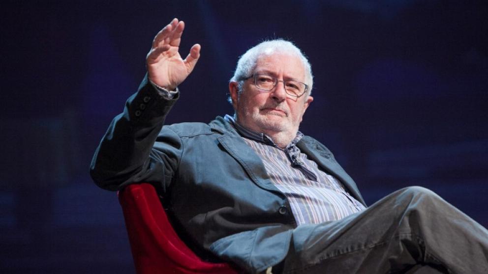 Terry Eagleton in a red chair with his hand up