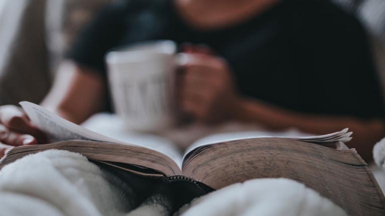 Person reading a book on their lap with a mug
