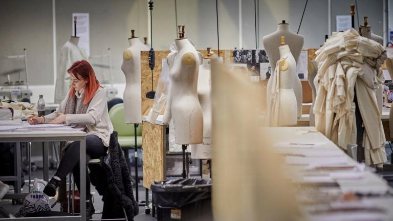 Woman working at a desk in a fashion student with mannequins around her 