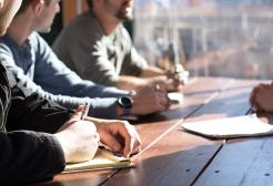 A table of students taking notes whilst discussing a project