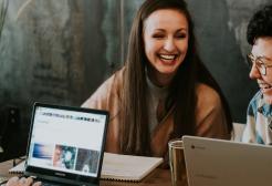 Three students gathered around a table working on laptops and chatting