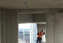 A worker wearing high-visibility gear installing exterior panels on a high-rise building