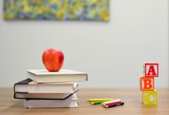 An apple on top of a stack of books, pencils and ABC building blocks
