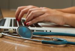 A person works at a laptop with a stethoscope beside them