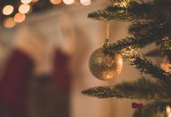 Christmas tree gold bauble hanging on a branch, with a blurred, warm-toned background