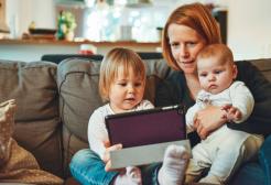 Mum sat on a sofa with her two young children watching an iPad