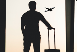 A person stands with luggage and watches a plane take off