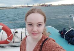 A landscape image of Lucy taking a selfie with a seafront in the background.
