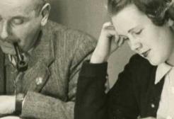 Black and white photo of a man and a woman reading or writing at a table, with the man smoking a pipe