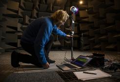 Crouched student working on equipment in the anechoic chamber, Newton Building, University of Salford