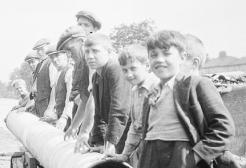 Archive image: A black and white photo shows a group of men and boys standing beside a large pipe for the canal.