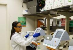 a lady in a white coat and blue gloves uses specialist equipment with a monitor