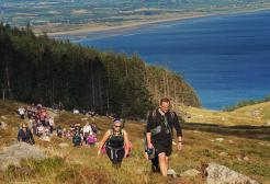 Numerous walkers ascending a hillside with a lake in the background