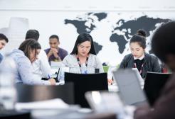 Students working in a group around a table with laptops and a map of the world behind them
