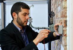 A researcher using a screwdriver to adjust a sensor hardware a brick wall inside the University of Salford's Energy House Lab