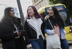 Three students walking around Manchester city centre alongside a tram