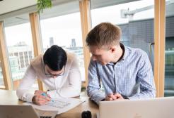 Two professionals working together in a planning meeting, each using a laptop