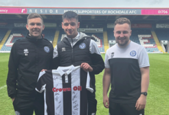 Three men posing with a football shirt at a football grounds.