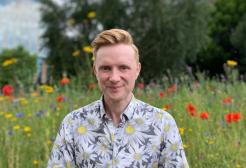 BBC's Owain Wyn Evans poses in a field of flowers. 