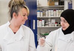 Two women in lab coats look at each other holding equipment in a lab. 