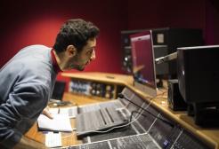 Student in recording studio surrounded by speakers and production equipment