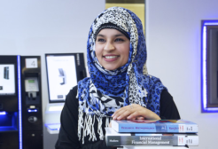 Salford student smiling holding a pile of business books