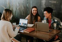 3 colleagues in conversation at a table with laptops
