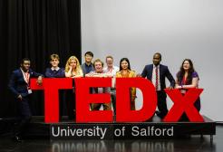 TEDxUniversityOfSalford sign with speakers behind it.