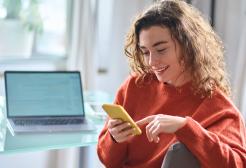 Person using their mobile phone next to a laptop