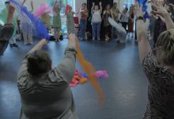 People are stood together in a hall taking part in a workshop waving around coloured scarves