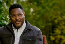 A man sat on the grass sketching looking over the camera