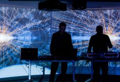 Two people at the Science and Industry museum looking at a big screen with an image of soundwaves