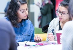 Two Salford students engaged in discussion, looking over notebooks during a seminar