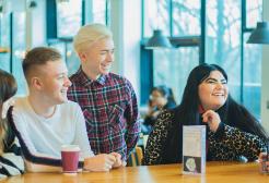 Five students socialising around a table in Maxwell Café, University of Salford