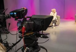 Two students presenting a talk show whilst another student films them in our TV studios