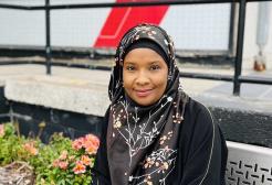 Aishatu Mohammed sat on bench in front of Maxwell Building, home of Salford Business School