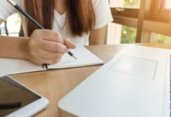 Student studying with a pen and paper at a laptop