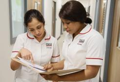 Two nursing students looking over nursing records in paper folder together